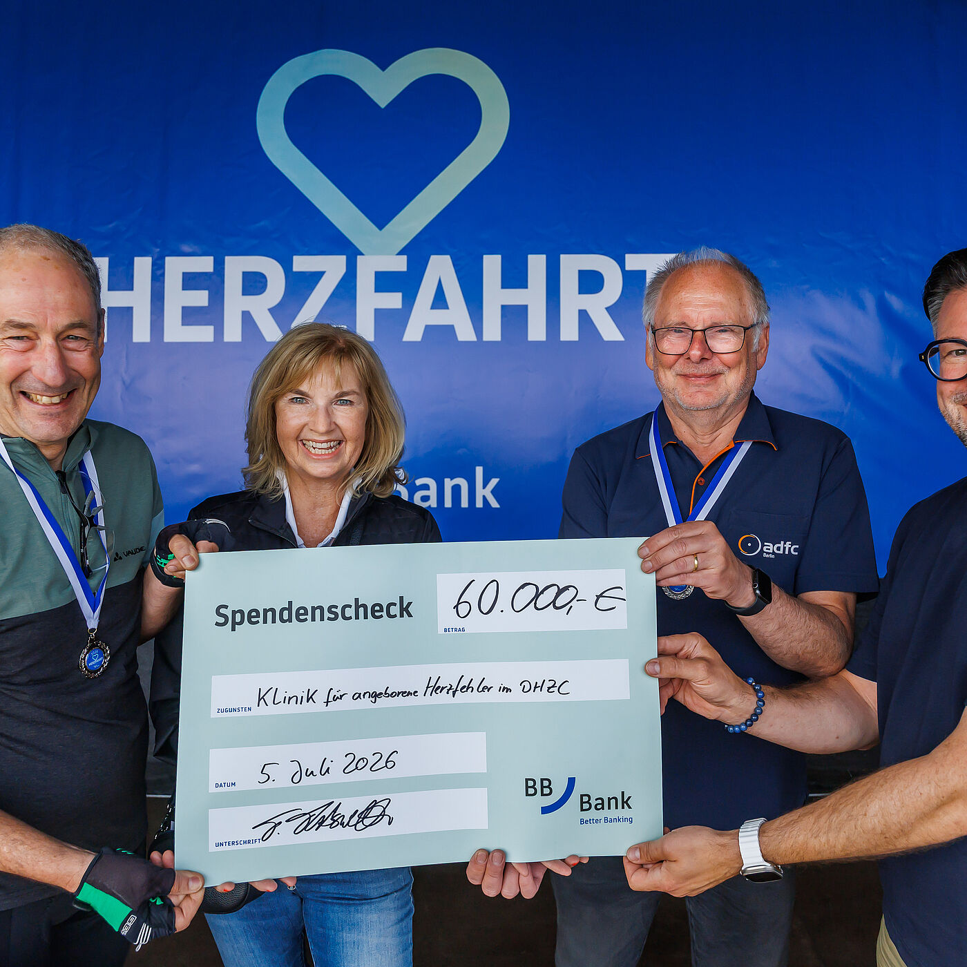Vier Menschen halten einen Spendencheck über 60.000€ bei der HerzFahrt