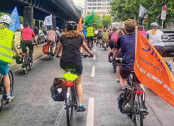 Respect Cyclists am 04. Juni Richtung Friedrichshain-Kreuzberg Eine Gruppe Radfahrende fährt mit Fahnen auf einer Fahrbahn Richtung Kreuzberg. Links im Bild ist die oberirdische U-Bahnlinie 1 zu sehen.