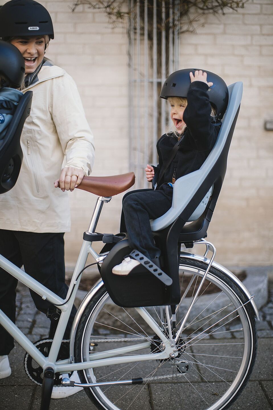 Praktisch: Kindersitze hinten Ein Kind mit Helm sitzt im Kindersitz hinten, das Fahrrad hält eine Frau mit Helm