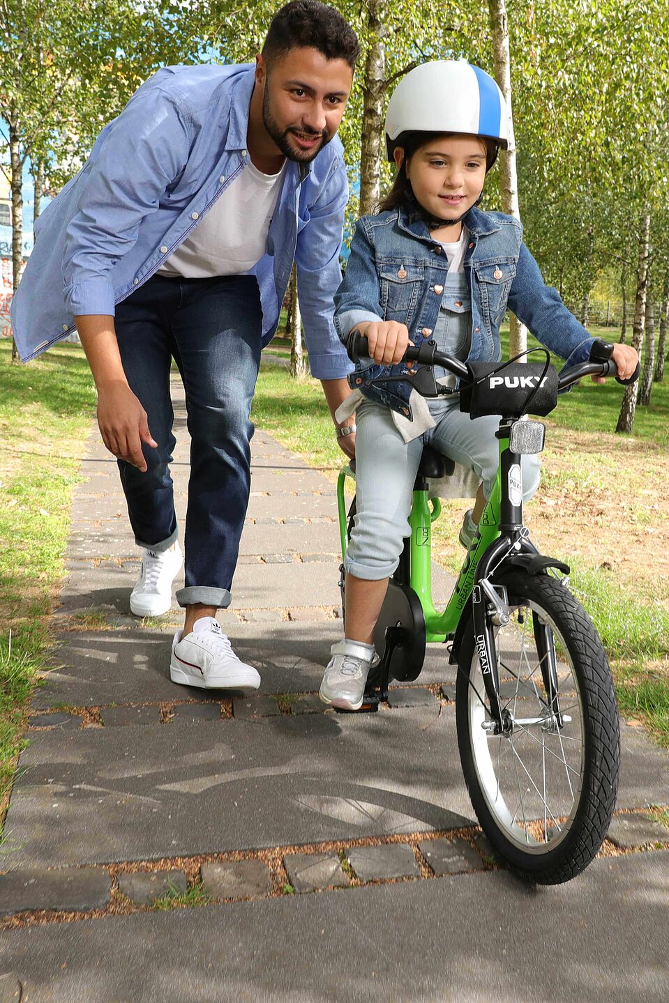 Kind lernt Radfahren Ein Mann unterstützt ein Mädchen beim Radfahrenlernen.
